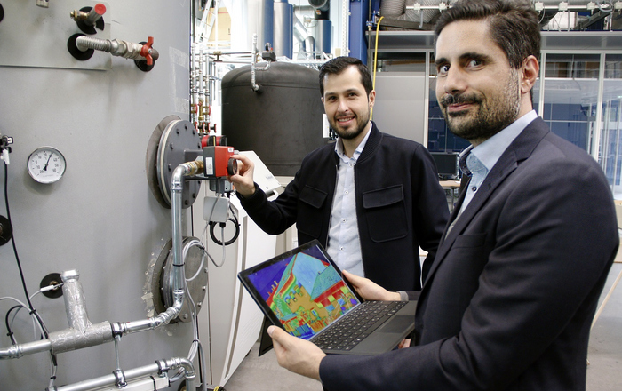 Prof. Dr. Rainer Gasper (rechts) und Mitarbeiter Oscar Villegas Mier (von rechts) vor einer Heizungsanlage. Prof. Gasper hält ein Laptop in den Händen auf dem die wärmeverteilung in einem Haus zu sehen ist.
